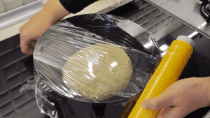 Proofed pastry dough that has doubled in size in a bowl covered with plastic wrap.