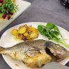 A tray of golden roasted sea bream with baby potatoes and onions, garnished with lemon.