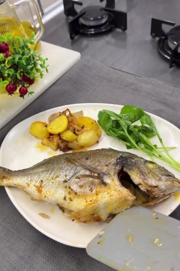 A tray of golden roasted sea bream with baby potatoes and onions, garnished with lemon.