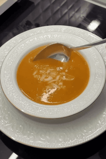 A steaming bowl of creamy roasted Turkish tomato soup (Domates Çorbası) topped with melted kashar cheese and a sprig of fresh thyme.