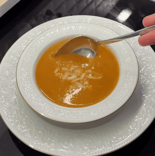 A steaming bowl of creamy roasted Turkish tomato soup (Domates Çorbası) topped with melted kashar cheese and a sprig of fresh thyme.