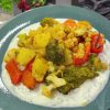 A vibrant platter of roasted spiced winter vegetables including cauliflower, broccoli, and chickpeas, served over a creamy bed of garlic yogurt and fresh dill.