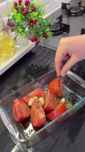 Chopped tomatoes and whole garlic cloves with thyme in an oven-safe dish for roasting.