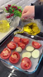 Halved tomatoes, onion rings, and garlic on a baking tray seasoned with thyme and olive oil for roasting.