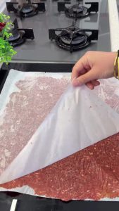 Rolling the thin meat mixture into a tight cylinder before placing it in the oven.