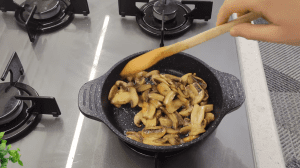 Sliced white mushrooms being sautéed in a skillet until golden brown and flavorful.