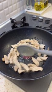 Sautéing diced chicken breast in a skillet with oil until golden brown.