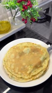 Transferring the hot, freshly cooked Kaygana pancake onto a serving plate, ready for breakfast.