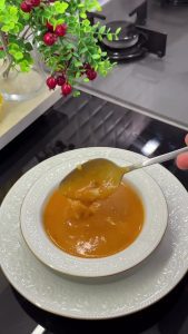 Ladling the hot roasted tomato soup into a bowl and topping it with a generous amount of grated kashar cheese.
