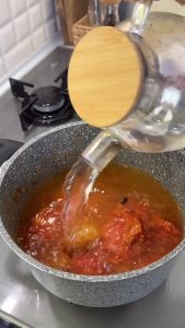 Adding water to the roasted vegetable mixture and letting it simmer on medium heat.