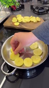 Slicing peeled potatoes into uniform medium-thick rounds for even cooking.