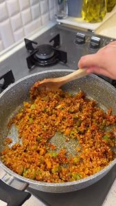 Adding coarse bulgur wheat to the pot and stirring with the seasoned paste and butter.