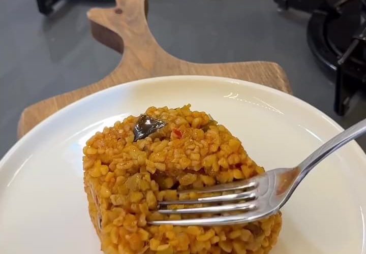 A close-up shot of fluffy Turkish bulgur pilaf with visible fried eggplant and green peppers.