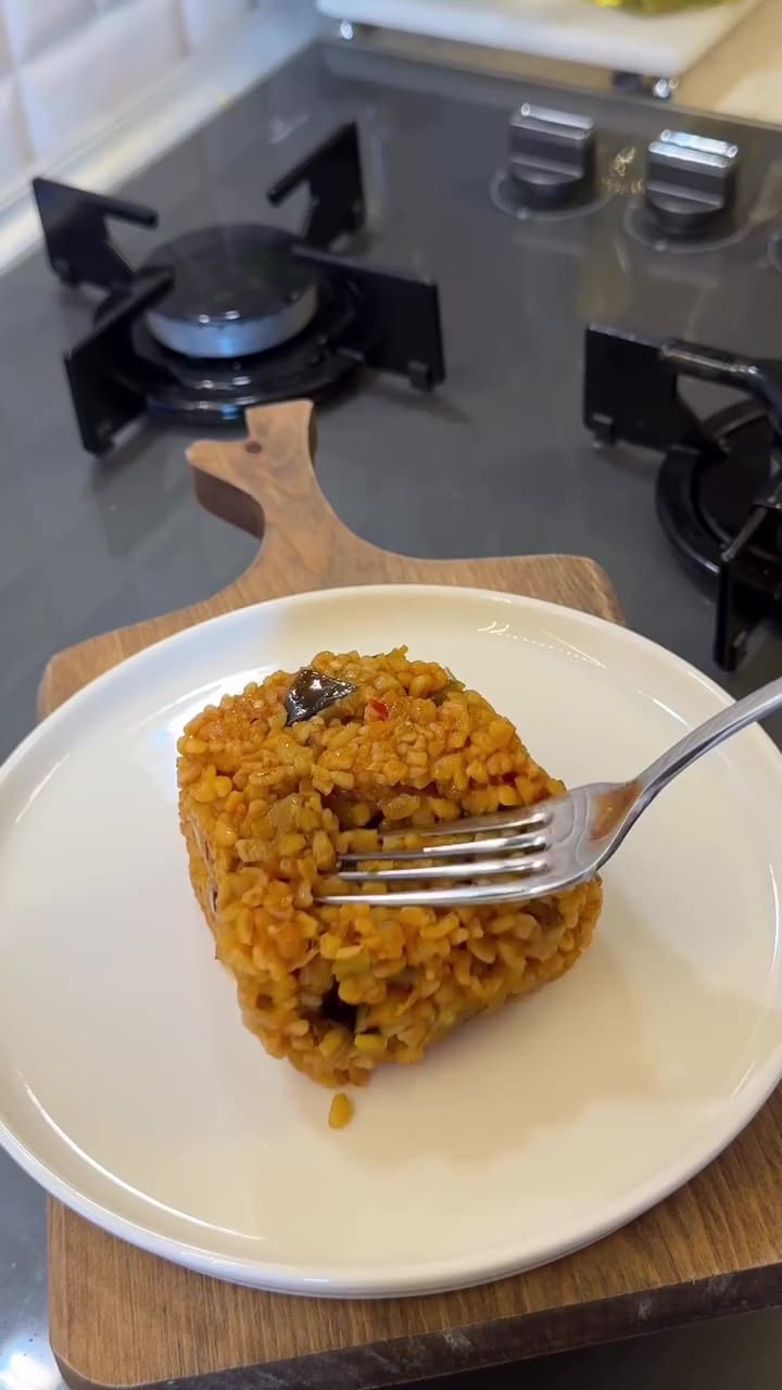 A close-up shot of fluffy Turkish bulgur pilaf with visible fried eggplant and green peppers.