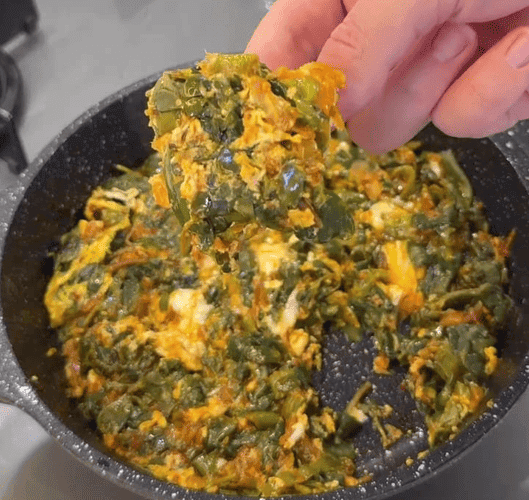 A healthy skillet of sautéed purslane and peppers topped with a cooked egg.