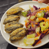 A delicious plate of Black Sea style stuffed fried anchovies (Hamsi Kusu) served with lemon wedges and fresh greens.