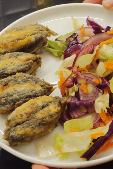 A delicious plate of Black Sea style stuffed fried anchovies (Hamsi Kusu) served with lemon wedges and fresh greens.