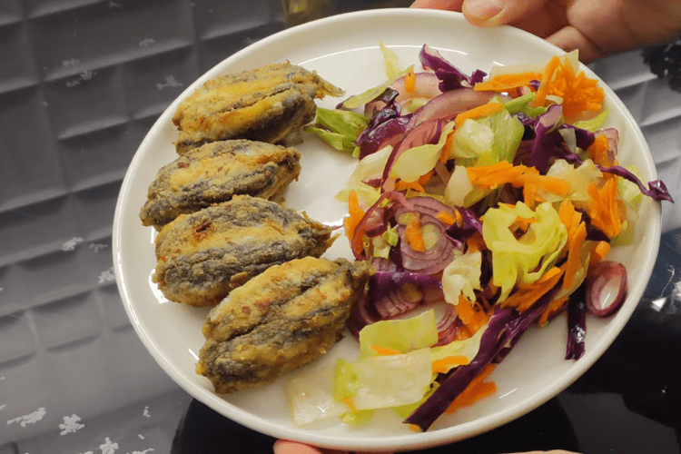 A delicious plate of Black Sea style stuffed fried anchovies (Hamsi Kusu) served with lemon wedges and fresh greens.