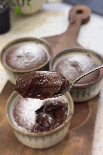 A warm chocolate soufflé with a molten center being opened with a spoon.