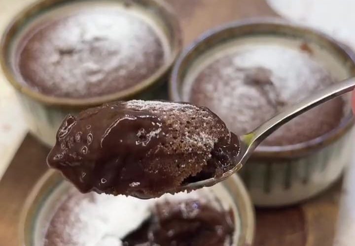 A warm chocolate soufflé with a molten center being opened with a spoon.