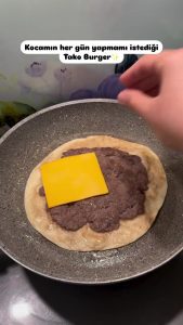 Placing a slice of yellow cheddar cheese over the cooked burger meat in the pan.