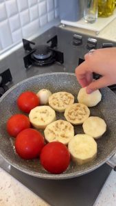 Adding peeled and sliced eggplant rounds to the pan with tomatoes.