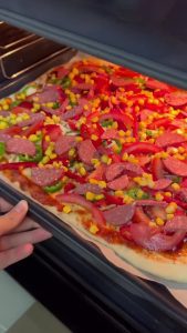 Adding a generous second layer of kashar cheese to the pizza during the final bake.