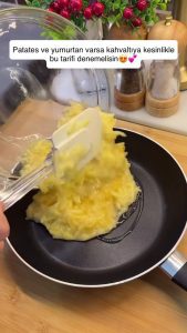 Cracking two fresh eggs over the dry grated potatoes in a glass bowl.