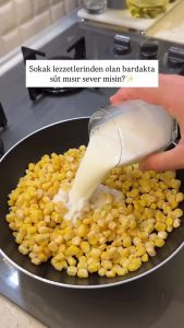 Adding frozen sweet corn and a cup of milk into a frying pan to start the cooking process.