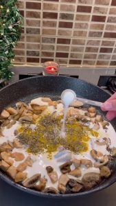 Pouring heavy cream and adding yellow curry powder to the pasta sauce.