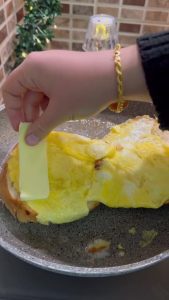 Adding slices of kashar cheese and salami to the breakfast sandwich.