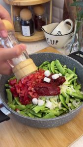Pouring olive oil and adding sugar cubes to the one-pot green bean mixture.