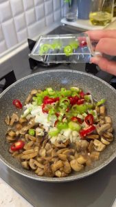 Adding diced onions, red capia, and green peppers to the browned mushrooms.