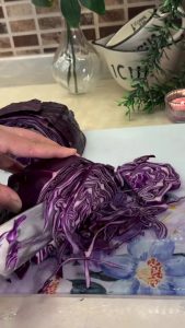 Sprinkling coarse rock salt over a bowl of sliced red cabbage.