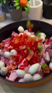Adding whole shallots and chopped peppers to the meat in the tray.