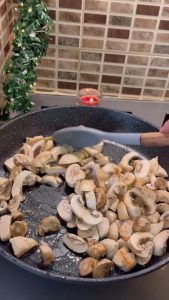 Adding sliced white button mushrooms to the pan with cooked chicken.