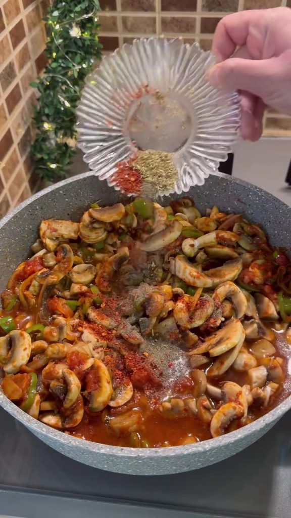 Adding red pepper flakes, oregano, and water to the mushroom sauté.