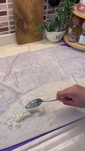 Placing crumbled white cheese on the edge of the sauced yufka sheet.