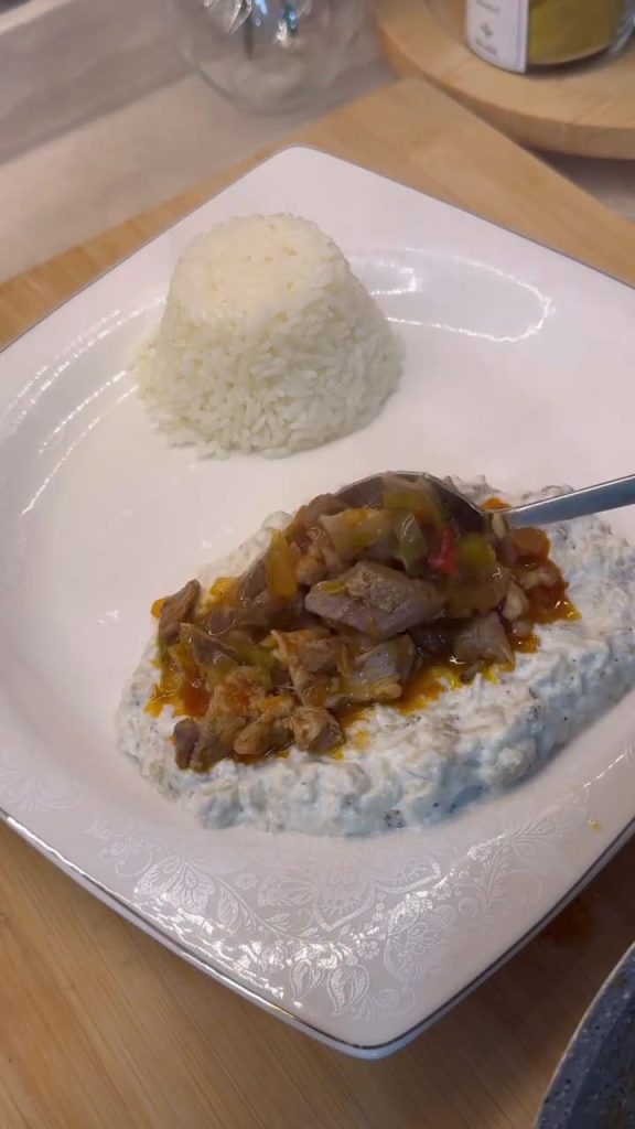 A plate of Alinazik Kebab featuring tender lamb cubes over smoky roasted eggplant and garlic yogurt puree.