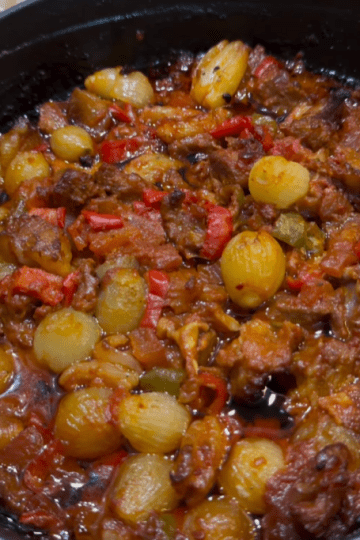 A traditional Turkish Belen Tava with roasted lamb, shallots, and peppers in a clay dish.