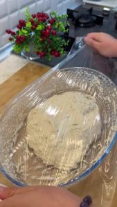 Bread dough resting and rising in a glass bowl covered with plastic wrap for 30 minutes.