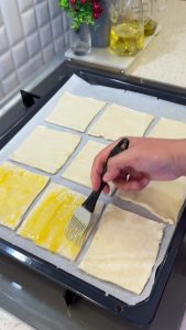Brushing the edges of the puff pastry rectangles with beaten egg yolk for a golden crust.