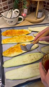 Brushing red pepper infused oil on eggplant slices before roasting.