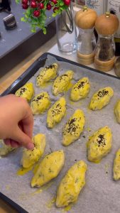 Brushing the tops of the shaped dill pastries with egg yolk on a baking tray.