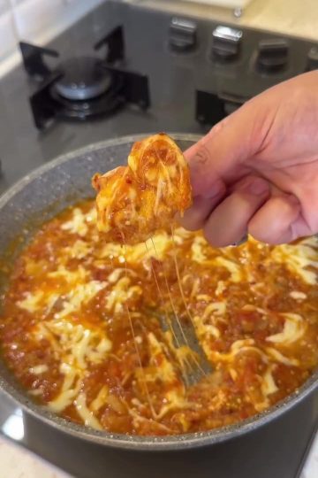 A skillet of mashed tomatoes and eggplant topped with melted kashar cheese.