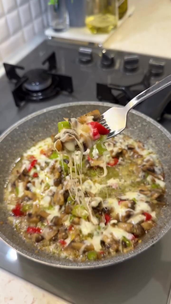 A close-up of sautéed mushrooms and peppers topped with melted, bubbly kashar cheese.