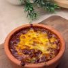 A bubbly, golden-brown cheesy mushroom casserole served in a traditional clay pot.