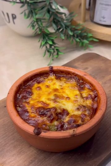 A bubbly, golden-brown cheesy mushroom casserole served in a traditional clay pot.