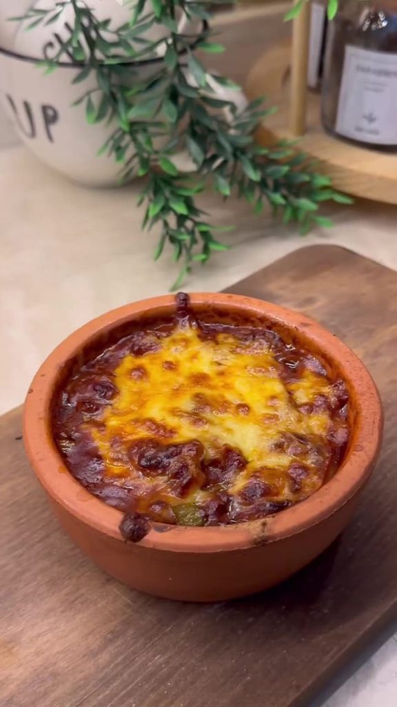 A bubbly, golden-brown cheesy mushroom casserole served in a traditional clay pot.
