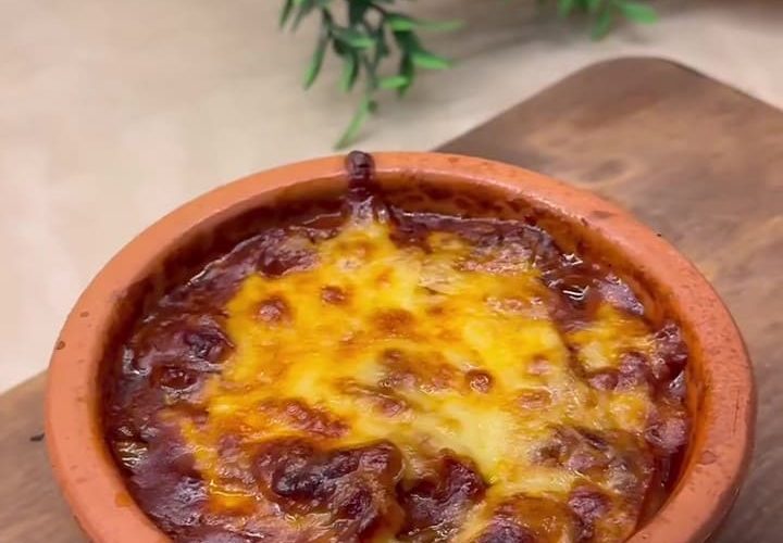 A bubbly, golden-brown cheesy mushroom casserole served in a traditional clay pot.